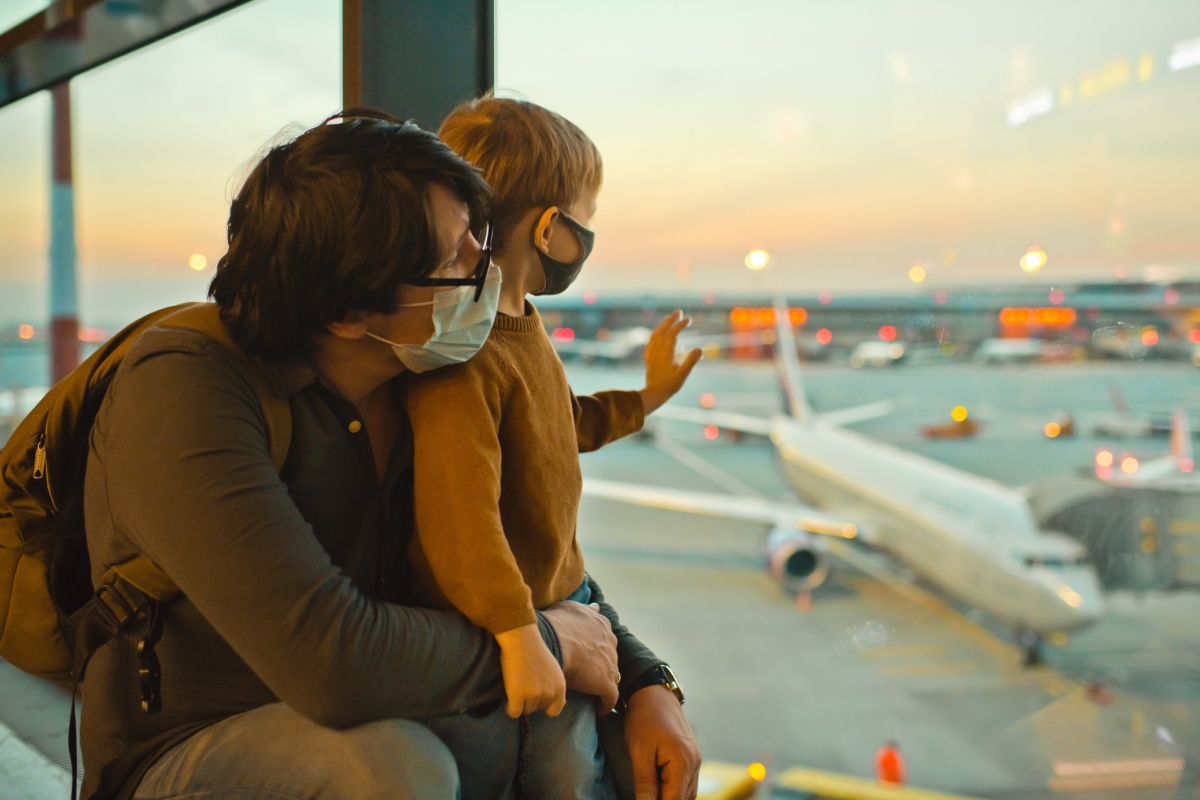 Vater und Sohn mit Gesichtsmasken schauen am Flughafen aus einem großen Fenster