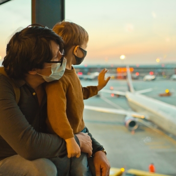 Vater und Sohn mit Gesichtsmasken schauen am Flughafen aus einem großen Fenster